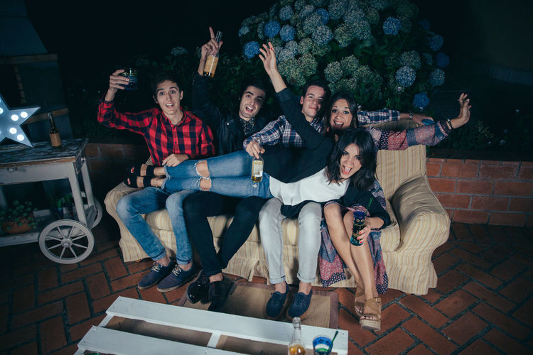 High angle portrait of cheerful friends on sofa at patio during night