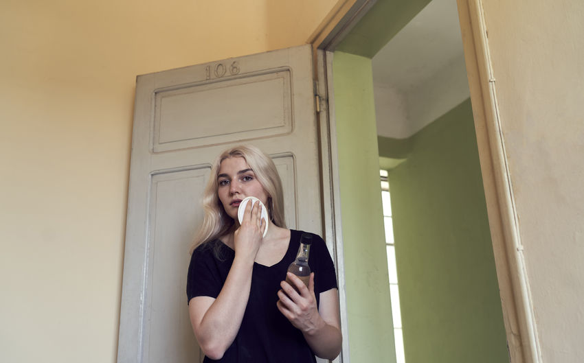 Woman applying cleansing lotion on her skin in hotel room interior