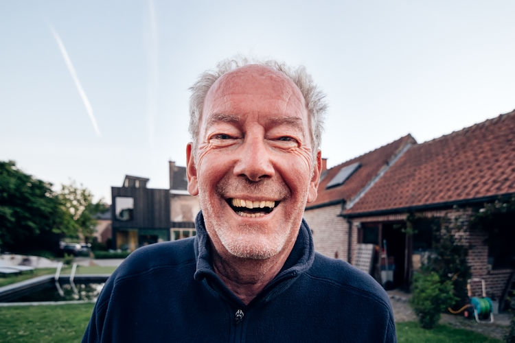 Portrait of elderly man laughing satisfied and happy in front of his house