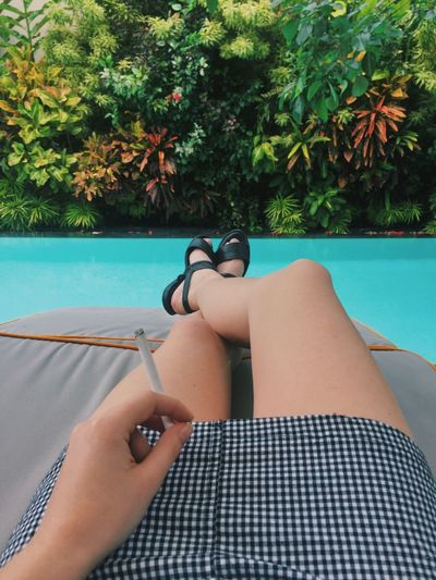 Low section of woman with cigarette sitting on chair by swimming poll