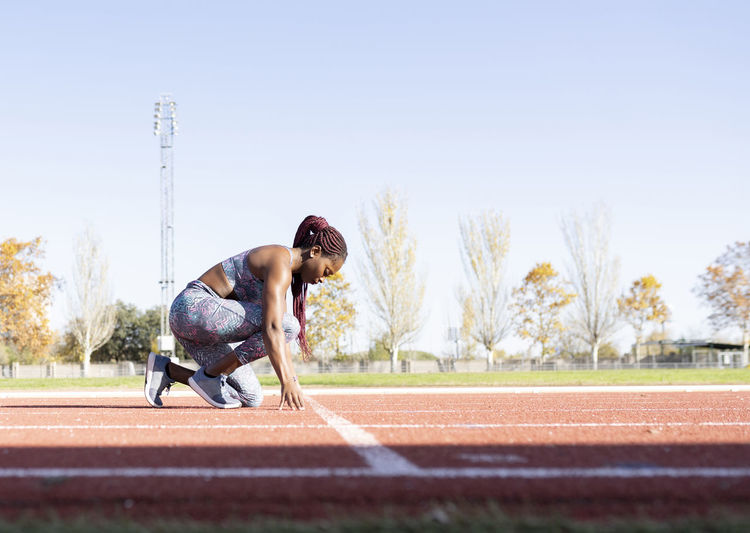 Female sportsperson in starting position on sports track during sunny day