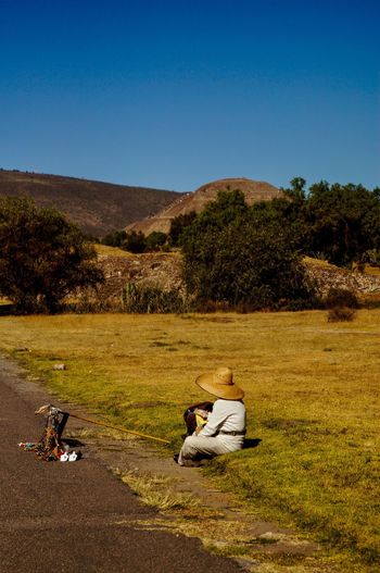 Man selling souvenirs at roadside while sitting on grass against sky