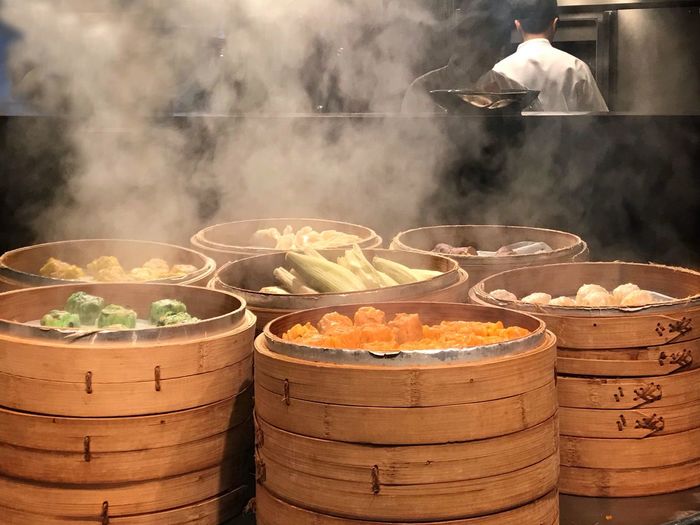 Food in bamboo steamers on table in kitchen with man in background
