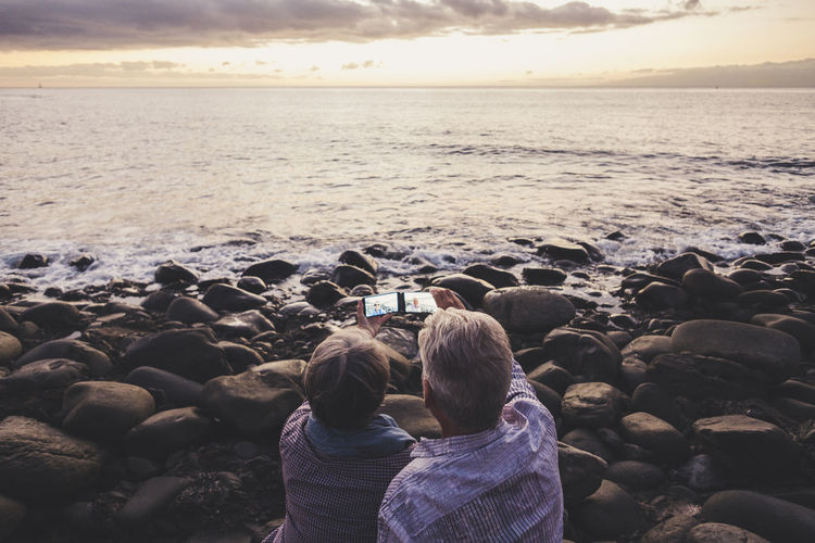 Rear view of couple taking selfie at rocky shore