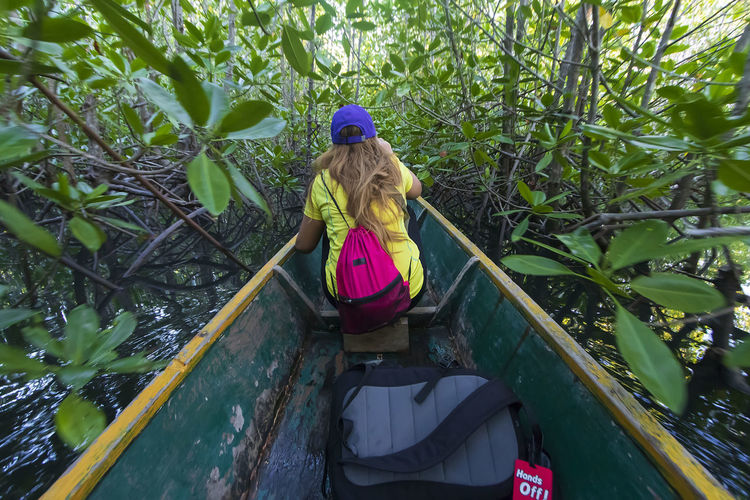Rear view of woman sitting in abandoned boat amidst plants 