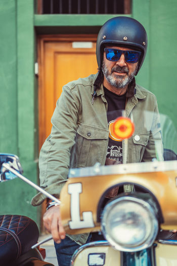 Bearded mature man in helmet and glasses sitting on custom motorcycle with many headlights on city street