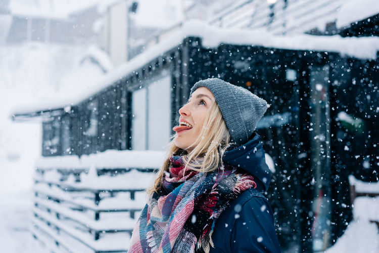 A young cheerful woman fools around like a child in a snowfall and catches snowflakes with tongue.