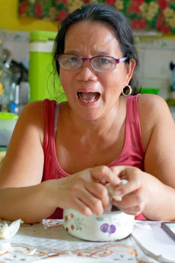 Portrait of mature woman screaming while sitting by table at home