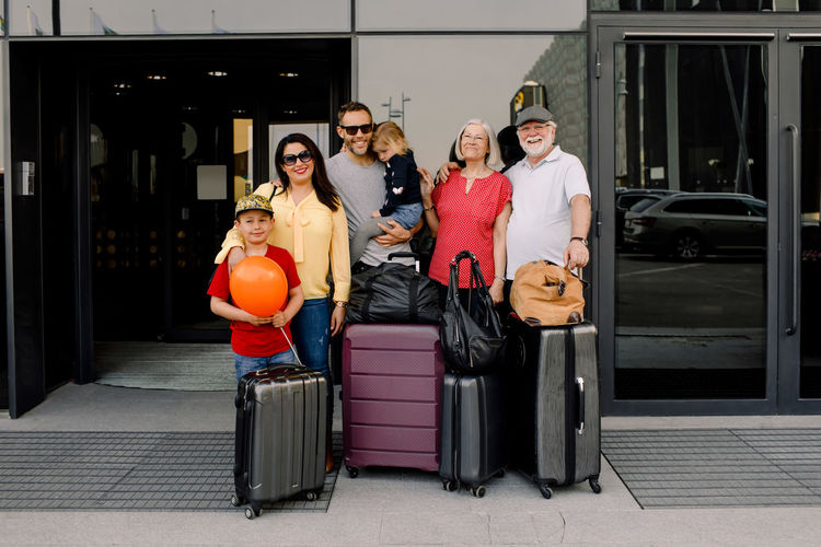 Portrait of happy family with luggage standing at hotel entrance