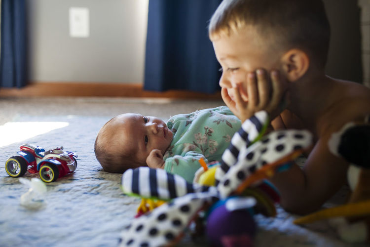 Baby girl looking at brother while lying on bed