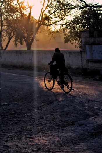 Man riding bicycle on footpath during sunset
