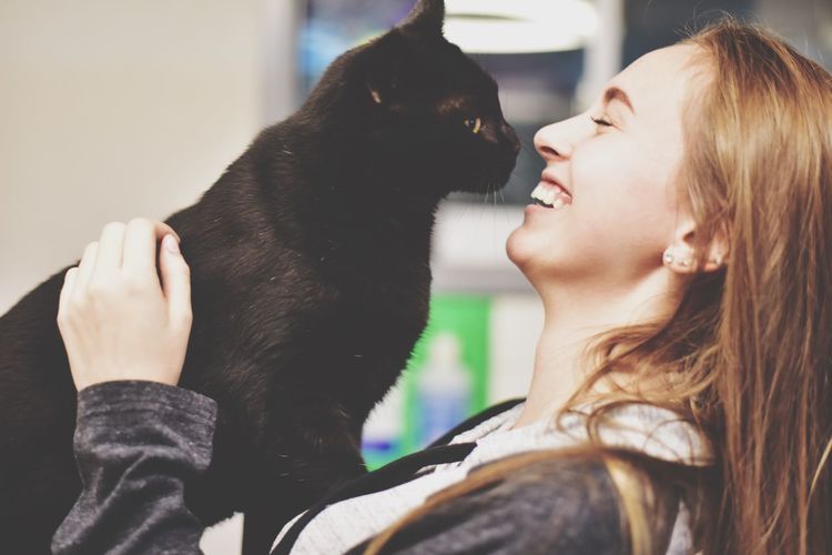 Smiling woman playing with black cat at home
