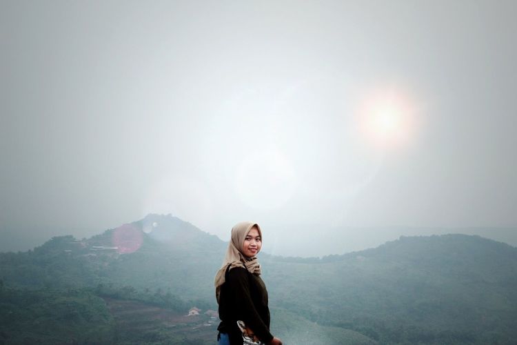 Portrait of young woman standing on mountain against sky