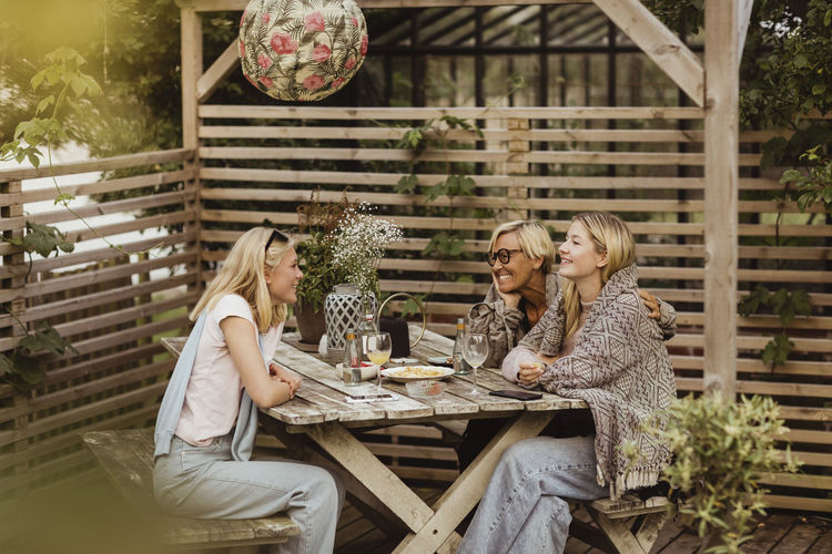 Smiling female friends spending time with grandmother at table in front yard