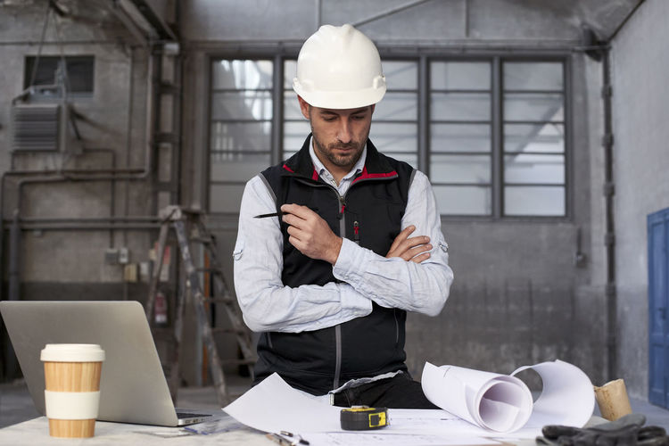 Male engineer thinking while analyzing blueprint on table in building