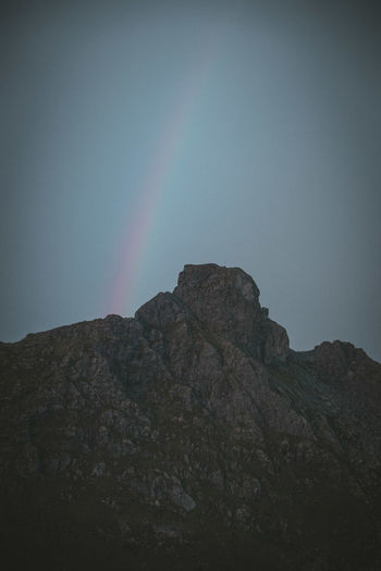Low angle view of rocky mountain against sky and rainbow