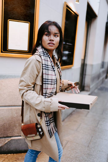Portrait of young woman using phone while standing against building