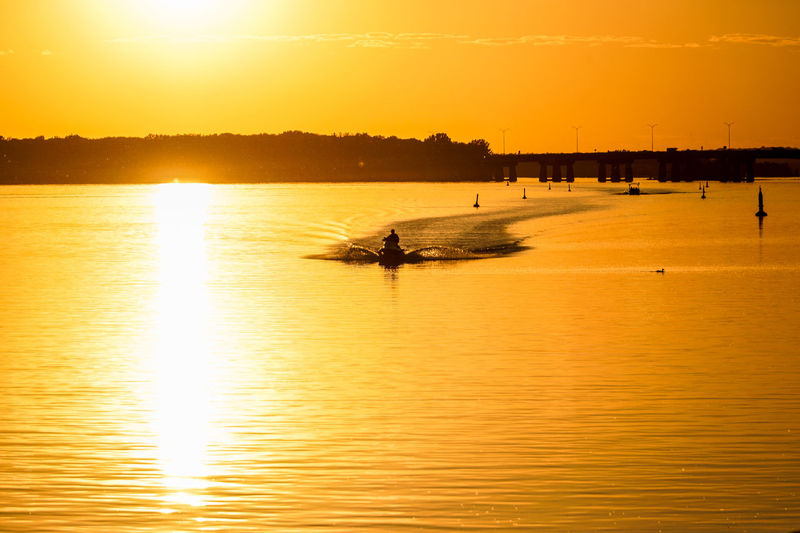 Silhouette person jet skiing in lake against orange sky during sunset