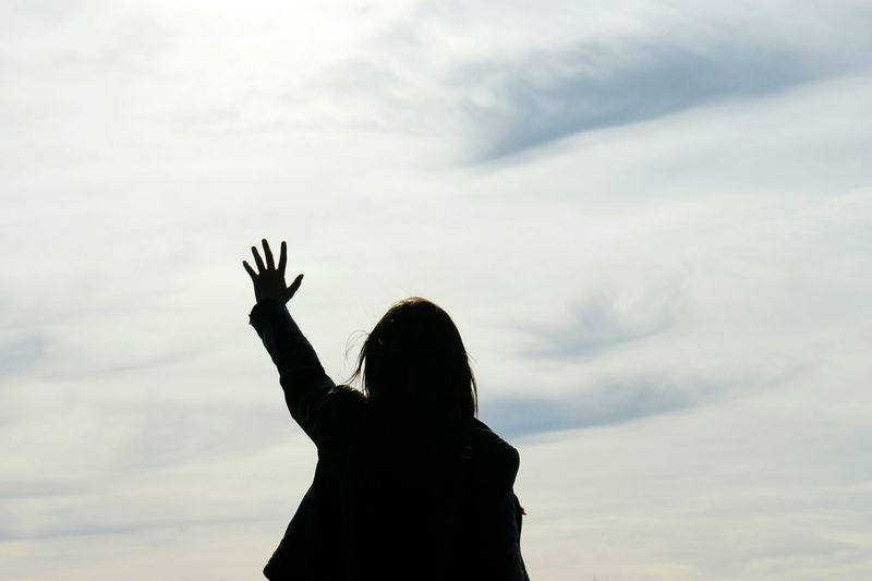 Silhouette woman with hand raised against sky