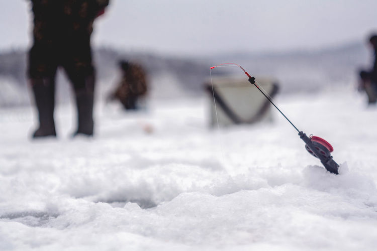 Fishing rod by hole on snow with woman standing in background