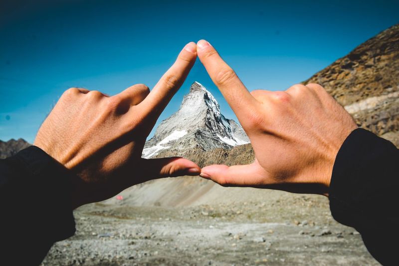 Cropped hands making triangle against mountain