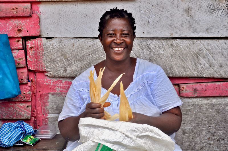Portrait of smiling vendor selling corns against wall