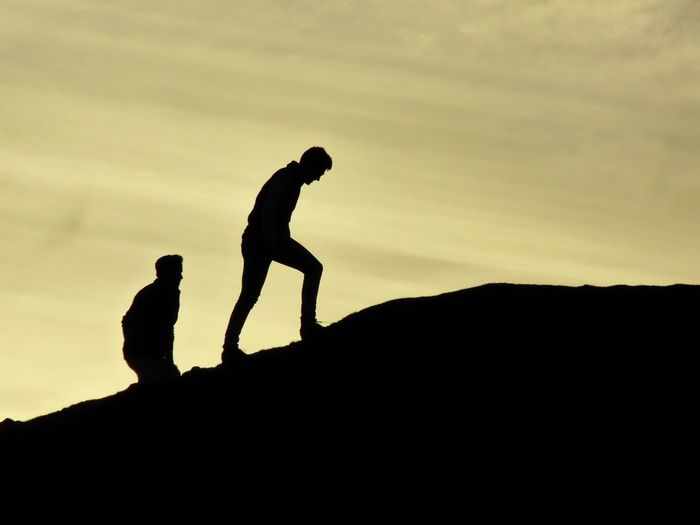 Silhouette men climbing mountain against sky