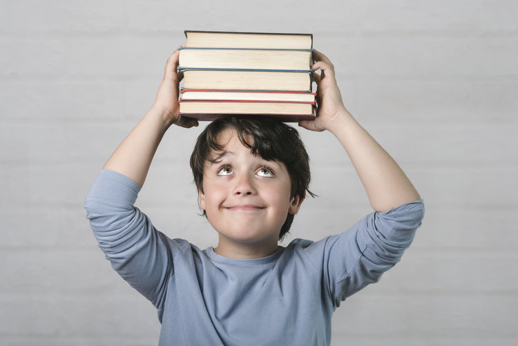 Portrait of boy holding book against wall