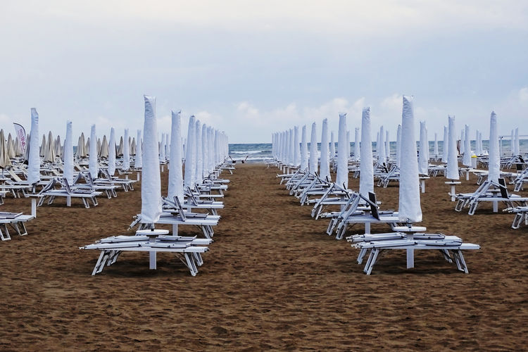 Empty chairs and beach umbrellas against sky