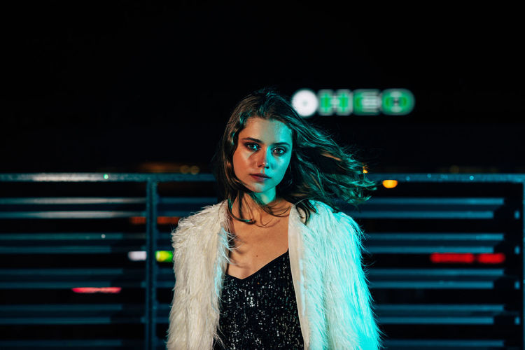 Portrait of young woman standing outdoors against at night