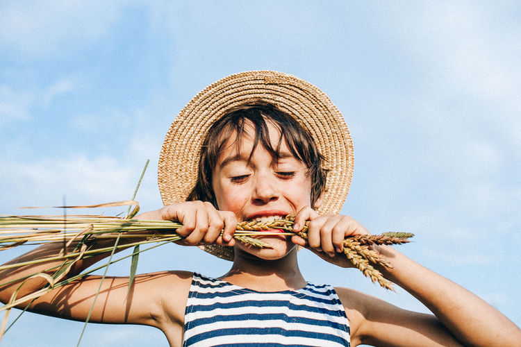 Boy biting crop against sky