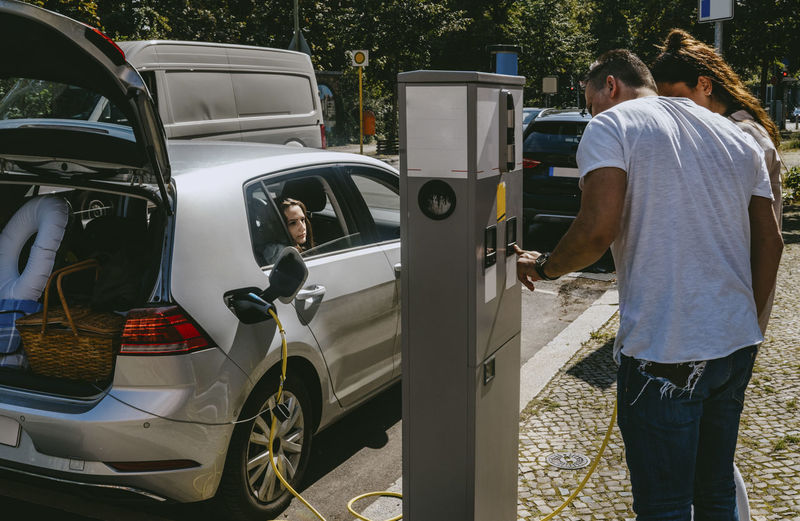 Mother and father checking charging of electric car at gas station