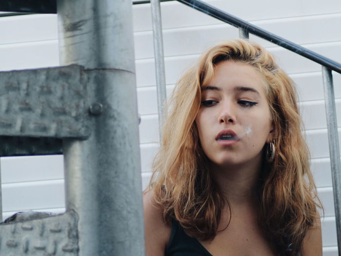 Young woman exhaling smoke while sitting on stairs