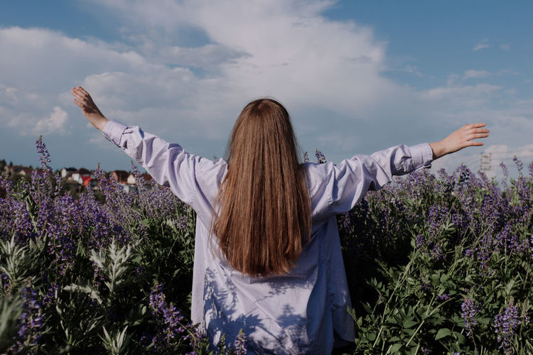 Unrecognizable woman with hands up outstretched arms in field of purple flowers
