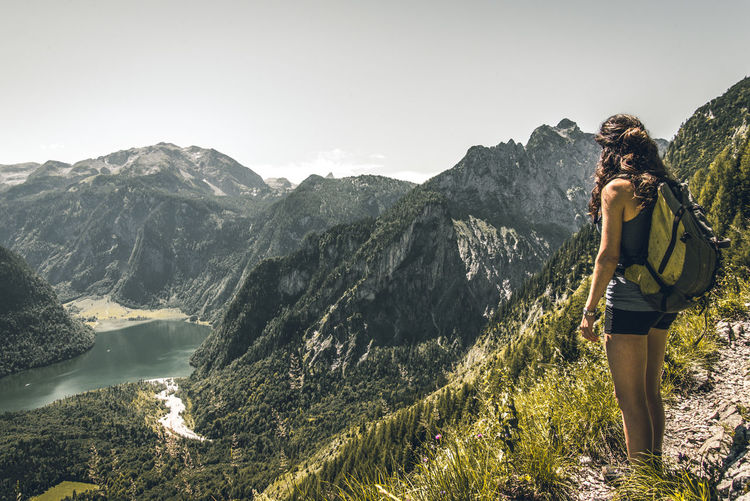 Side view of woman with backpack standing on mountain against sky