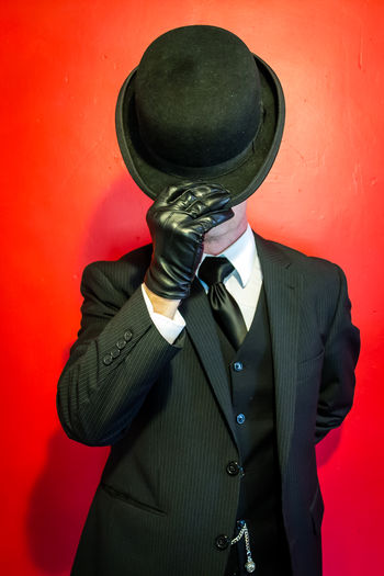 Man covering face with hat while standing against wall