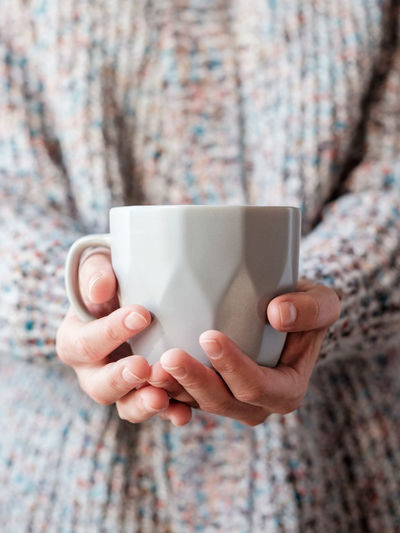 A woman dressed in a wool sweater on a cold day and holding a cup of warm tea in her hands.
