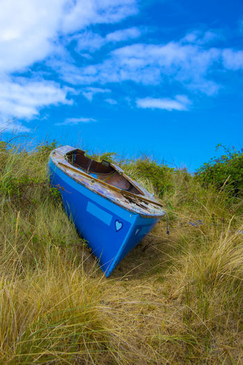 Boat moored on field against blue sky