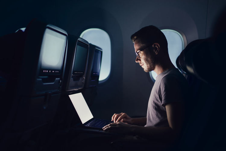 Man traveling by airplane. young passenger using laptop during night flight.