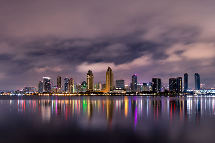 Illuminated buildings by river against sky