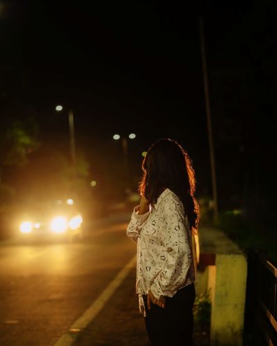 Side view of woman looking away while standing on street at night