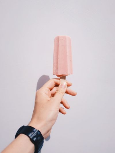 Close-up of hand holding ice cream cone against white background