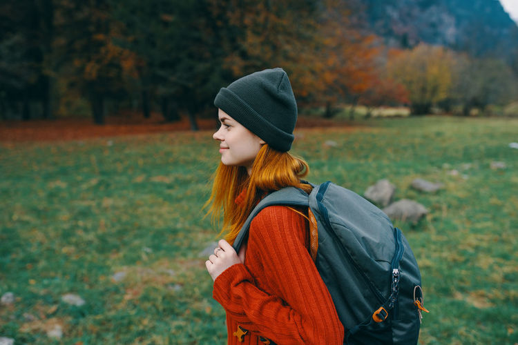 Young woman looking away while standing on field during autumn
