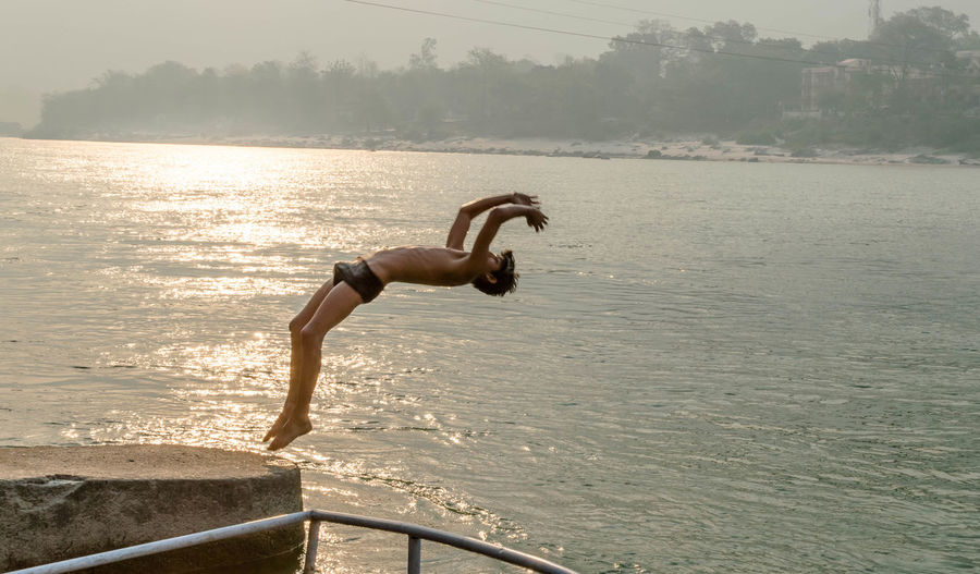 Full length of shirtless man jumping in river