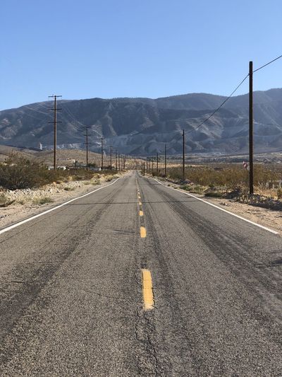 Empty road by mountain against clear sky