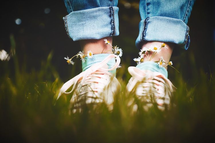Low section of woman with flowers wearing shoes and socks on grass