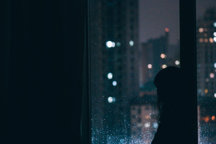Side view of man looking through window at night