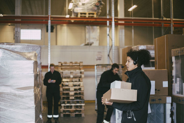 Female entrepreneur holding packages standing by colleagues at logistics warehouse
