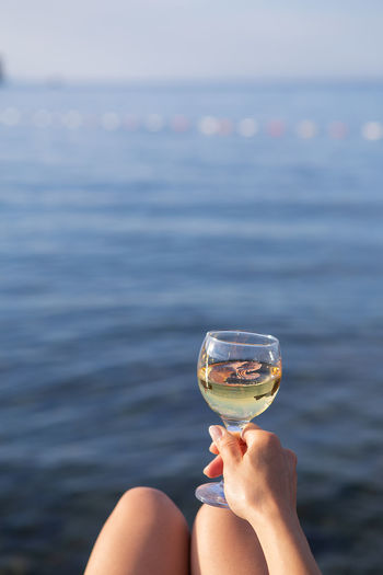 A girl holds in her hand a glass of white wine against the backdrop of a beautiful blue sea.