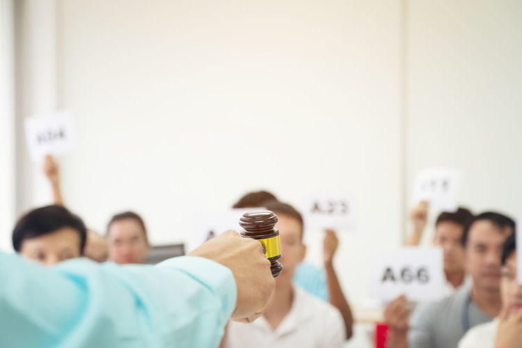 Cropped hand holding gavel against people during auction